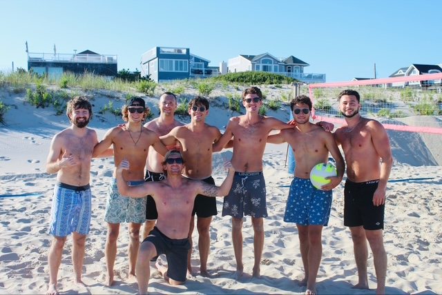 A team poses with the game ball in front of the beachfront houses